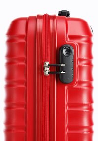 Red hard-shell suitcase with a textured surface, featuring a central zipper and a black combination lock on the side.