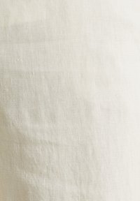 Gros plan sur un tissu en lin tissé beige clair avec des fils texturés visibles et de légères plis naturels.