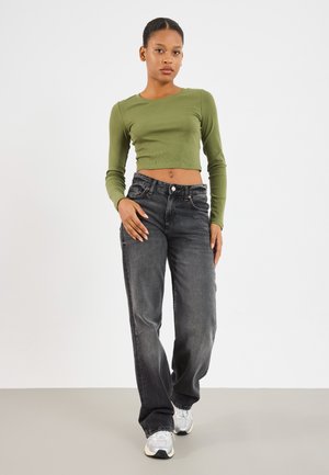 Zielony prążkowany crop top z długim rękawem zestawiony z czarnymi prostymi dżinsami. Model nosi jasnoszare sneakersy. Minimalistyczny design, neutralne tło.