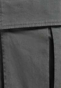 Grått tyg med en slät textur och subtila diagonala vävningsmönster, med sydda sömmar och en överlappande flikdetalj.