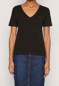 Svart bomulls T-shirt med V-hals och korta ärmar; har en liten logotyp på vänster bröst. Matchas med en blå denimkjol.