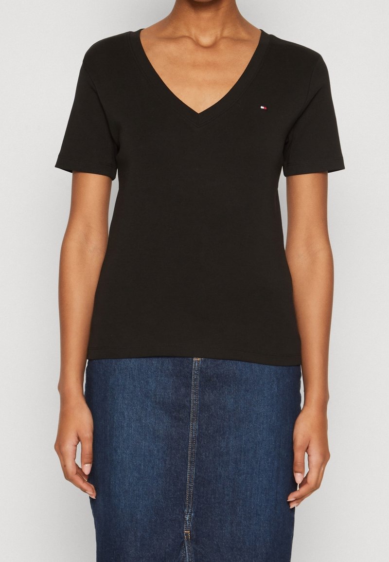 Svart bomulls T-shirt med V-hals och korta ärmar; har en liten logotyp på vänster bröst. Matchas med en blå denimkjol.