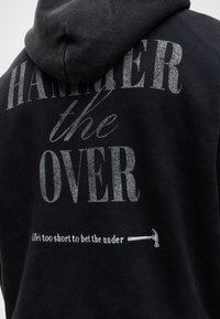 Черен суичър с голям сребърен текст "Hammer the Over" и по-малък текст "Life's too short to bet the under" с икона на чук.