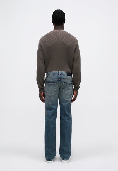 Καφέ πλεκτή ζακέτα με ραβδώσεις, συνδυασμένη με ανοιχτό μπλε τζιν παντελόνι κατευθείαν με πίσω τσέπες, φορεμένη με λευκά αθλητικά παπούτσια.