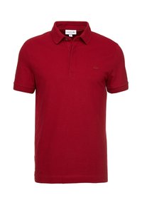 Polo en coton rouge avec col, manches courtes et un logo brodé discret sur la poitrine. Texture douce, coupe classique.