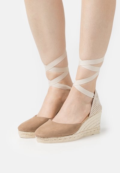 Sandali in suede color marrone chiaro con una prominente piattaforma in juta intrecciata. Cravatte in tessuto che incrociano sopra la caviglia. Texture liscia e design con punta chiusa.