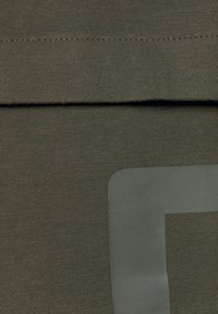 Tessuto elasticizzato verde oliva con un motivo a maglia testurizzato, caratterizzato da un accento liscio e lucido in forma rettangolare su un bordo.
