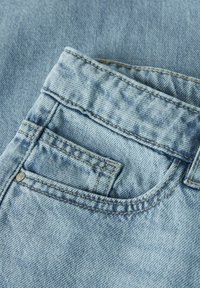 Jasnoniebieski materiał dżinsowy z wyraźną tylną kieszenią. Z widocznym przeszyciem i małym metalowym nitonem. Miękka tekstura.