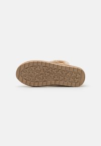 Chaussures de couleur beige avec une semelle en caoutchouc texturé, présentant un motif de rainures et d'accents en relief pour une meilleure adhérence et stabilité.