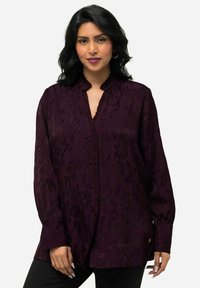Dark purple blouse featuring a textured floral pattern, a ruffled neckline, long sleeves with buttoned cuffs, and a decorative gold accent.