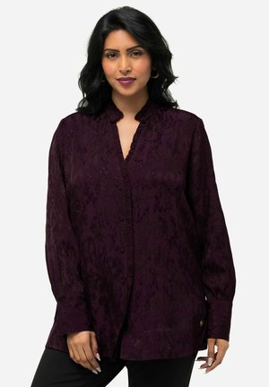 Dark purple blouse featuring a textured floral pattern, a ruffled neckline, long sleeves with buttoned cuffs, and a decorative gold accent.