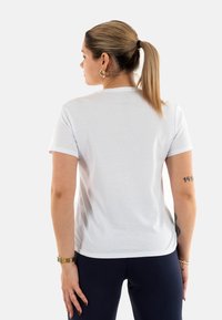 Camiseta blanca de manga corta en un corte relajado con escote redondeado. Textura suave sin patrones o acentos visibles. Diseño simple.
