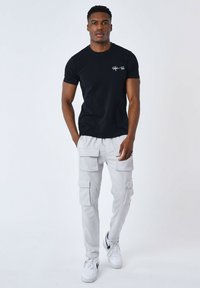 Camiseta negra de manga corta con logo blanco, combinada con pantalones cargo gris claro con múltiples bolsillos y zapatillas blancas.