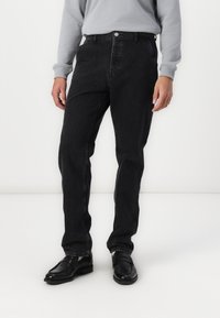 Sorte denim jeans med lige ben, som har en knaplukning, fem lommer og diskrete stikninger. Sammen med sorte sko.