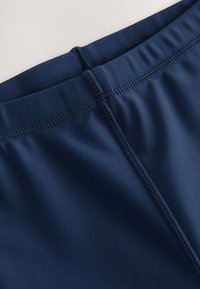 Marineblå atletikshorts med en glat tekstur, elastisk linning og flatlock-syning langs sømmene for holdbarhed.