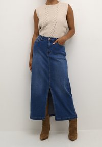 Ljusbeige ärmlös topp med ett texturerat mönster som är parat med en mörkblå denim maxi-kjol med en framficka. Bruna ankelstövlar.