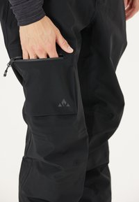 Zwarte waterdichte broek met een ritszak aan de zijkant, met een gestroomlijnd ontwerp en een textuurafwerking; logodetail op de zak.
