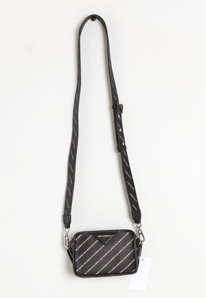 Bolso cruzado negro de Karl Lagerfeld con correa ajustable y patrón de logotipo en diagonal, colgado sobre un fondo blanco.