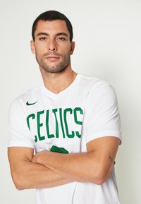 Kortærmet hvid T-shirt med stort grønt "CELTICS" tekst, letvægts bomuldsmateriale, rund halsudskæring og en afslappet pasform.