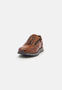 Scarpa in pelle marrone con superficie texturizzata, design con lacci, dettaglio con zip laterale e suola in gomma grigia, con accenti di cucitura lungo i bordi.
