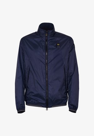 Marineblauwe lichtgewicht jas met rits, opstaande kraag, elastische manchetten en zoom, en een klein gebrandmerkt patch op de linkerborst.