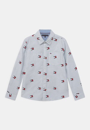 Lyseblå og hvide stribet skjorte med lange ærmer, knaplukning foran og spredte små røde, hvide og sorte rektangulære flagmønstre.