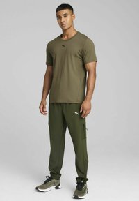 Conjunto de ropa deportiva de color verde oliva que incluye una camiseta de manga corta y pantalones cargo. Los pantalones tienen bolsillos con cremallera; los zapatos son negros con detalles en verde.
