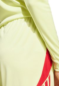 Lichtgele sporttop met rode accenten, voorzien van een geraffineerde tailleband en een subtiele merkteken. Gemaakt van een soepele, rekbare stof.
