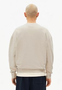 Beiger Pullover mit lockerem Schnitt, rundem Halsausschnitt und gerippten Bündchen. Glatte Textur, leicht tailliert und etwas kürzer geschnitten.