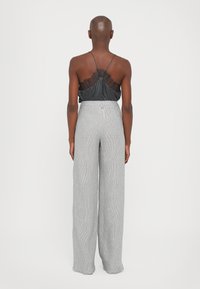 Black cami top with lace detailing at the back, paired with high-waisted, wide-leg grey striped trousers. Smooth texture, soft fabric.
