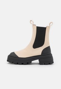 Botas Chelsea bege com painéis laterais elásticos pretos, ponteiras de borracha preta e sola grossa. Apresentam um acabamento texturizado e abas de puxar.