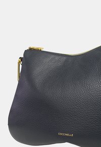 Borsa a spalla in pelle blu navy con una superficie testurizzata, dotata di una cerniera e accessori dorati, e un logo in rilievo sobrio.