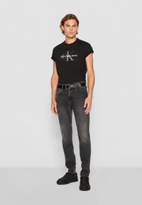 Camiseta negra de Calvin Klein Jeans de mangas cortas, jeans grises, cinturón negro y zapatos negros. Diseño ajustado, textura suave y minimalismo en la marca.