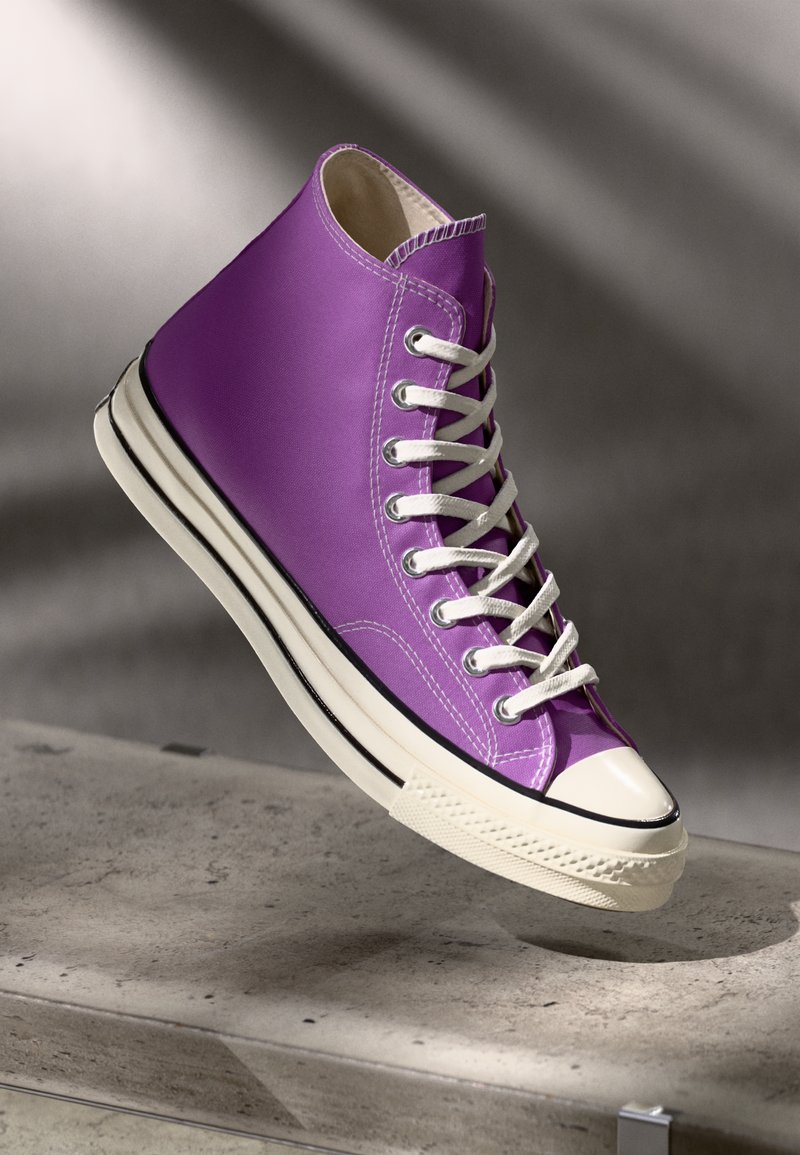 Purple high-top sneaker with white laces, rubber toe cap, and black stripe on the sole. Smooth fabric upper and padded collar.