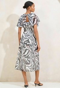 Haalikäärme, harmaa ja valkoinen zebra-kuosisessa mekossa on leijuvat hihat, avokseli takaosa-design ja virtaava siluetti. Yhdistetty mustiin liukuveneisiin.