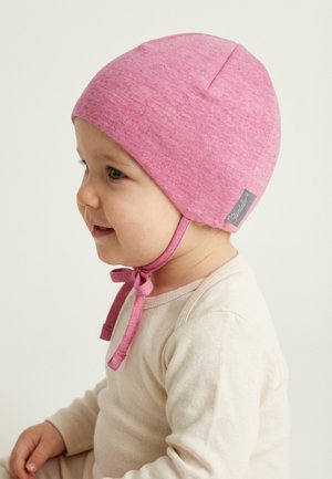 Toddler wearing a pink soft fabric hat tied under the chin and a cream long-sleeve top, facing left with a slight smile.
