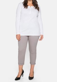 Haut en coton blanc à manches longues avec patte de boutonnage, associé à un pantalon léger gris clair avec revers et des talons hauts noirs. Design simple et ajusté.