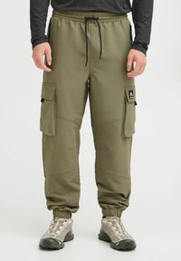 Pantalones cargo de color verde oliva con cintura elástica, cordón y múltiples bolsillos. Tejido suave con costuras visibles y puños elásticos.