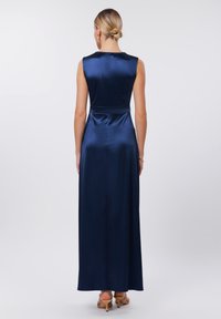 Robe maxi en satin marine avec design sans manches, taille ajustée et jupe fluide. Texture lisse avec un éclat subtil. Vue de dos montrant un minimum de détails.