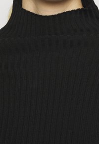 Svart ribbad turtleneck-tröja tillverkad av ett mjukt, elastiskt material. Har en hög krage och vertikal textur över hela materialet.