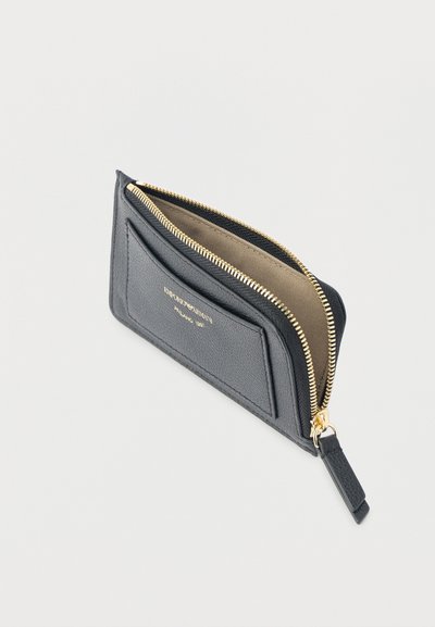 Μαύρο δερμάτινο πορτοφόλι με φερμουάρ σε χρυσό χρώμα και μπεζ εσωτερικό, με εξωτερική θήκη για κάρτες και ανάγλυφο κείμενο της μάρκας στην πρόσοψη.