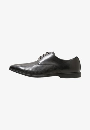 Chaussure habillée pour homme en cuir noir poli avec laçage à l'avant et détails perforés sur l'avant et les côtés, talon bas, vue de profil latéral.