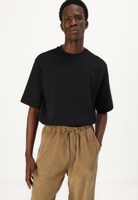 Sort kortærmet t-shirt med rund halsudskæring, parret med brune kordfløjlsbukser med elastisk talje og snøre-detaljer.
