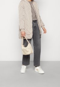 Ljusbeige vadderad jacka, grå topp, högmidjade mörka jeans, vita sneakers med beige detaljer och en liten krämfärgad handväska.
