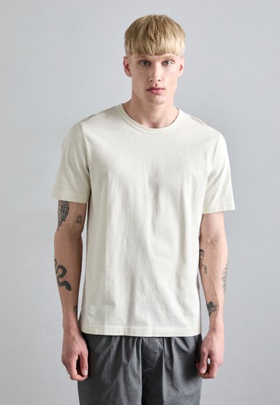 Crème katoenen t-shirt met een ronde halslijn en korte mouwen, met een relaxte pasvorm en een soepel textuur, gedragen met grijze shorts.