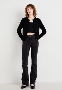 Črni pleteni cardigan s okroglim izrezom, sprednjim zapenjanjem in dolgimi rokavi. Nošen čez črno kratko majico in v kombinaciji z visokim pasom ter razširjenimi jeans hlačami.