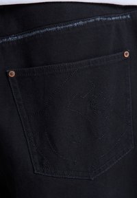 Sort denimstof med en baglomme med kontrastsyning, et logodesign og en kobbernitte-detalje.