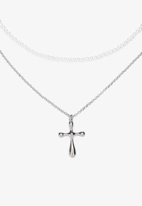 Collier en chaîne argentée avec un pendentif croix brillant, superposé à une chaîne de perles blanches. La croix présente un design arrondi et une texture lisse.