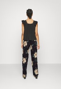 Czarna bezrękawnikowa bluzka z falbaniastymi ramionami w połączeniu z czarnymi spodniami w kwiatowy wzór z beżowymi kwiatami i zielonymi liśćmi.