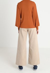 Rostrandig långärmad topp med puffärmar, kombinerad med beige vida byxor och marinblå sneakers; mjuk textur, avslappnad passform.